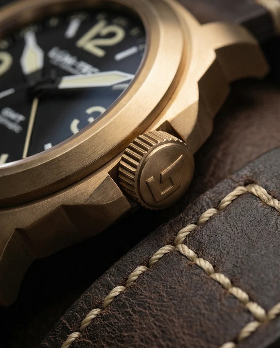 Macro shot of the Lum-Tec M94 Bronze No-Date GMT watch highlighting the fine brushed CuSn8 solid bronze case, engraved logo threaded crown, and premium brown Horween leather strap with cream stitching
